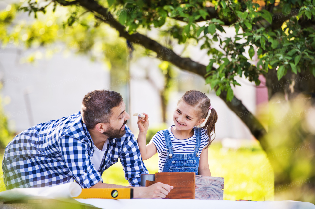 Father with a small daughter outside, making wooden birdhouse or bird feeder.