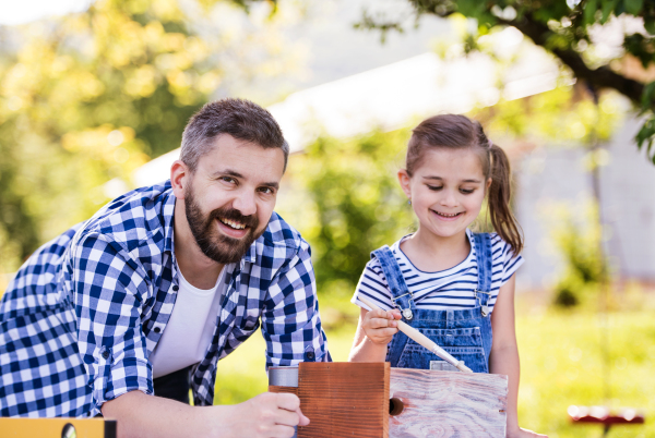 Mature father with a small daughter outside, painting. Wooden birdhouse or bird feeder making.