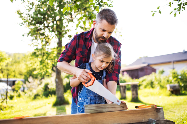 Father and a small daughter with a saw outside, making wooden birdhouse or bird feeder.