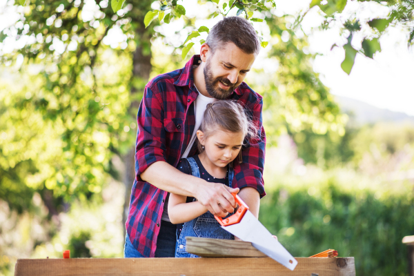 Father with a small daughter outside, making wooden birdhouse or bird feeder.