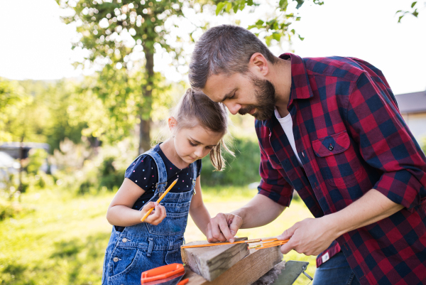 Handsome father with a small daughter outside, making wooden birdhouse or bird feeder.