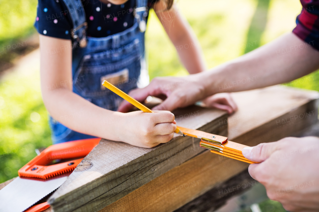 Unrecognizable father with a small daughter outside, making wooden birdhouse or bird feeder.