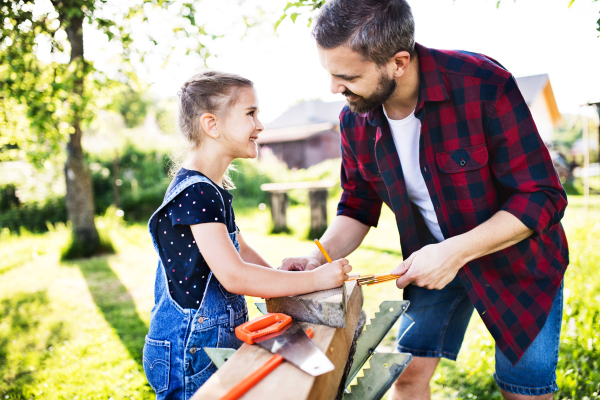 Father with a small daughter outside, making wooden birdhouse or bird feeder.