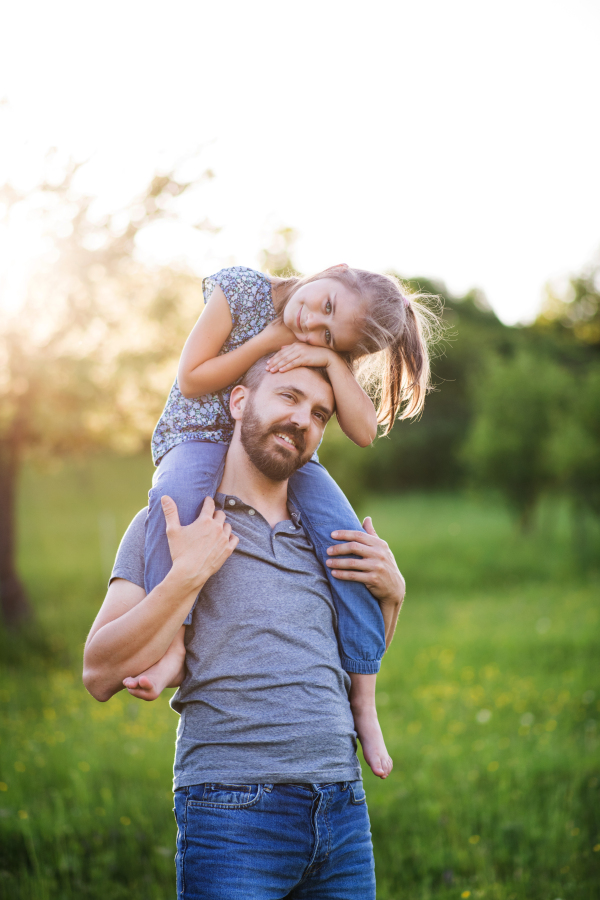 Mature father giving a small daughter a piggyback ride in spring nature.