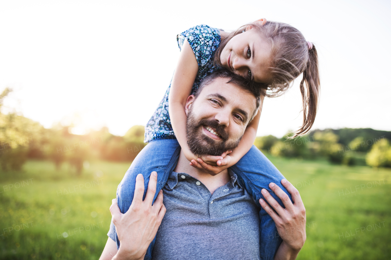 Mature father giving a small daughter a piggyback ride in spring nature.