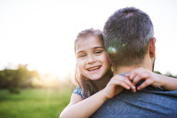 Unrecognizable father holding a small daughter in spring nature at sunset.