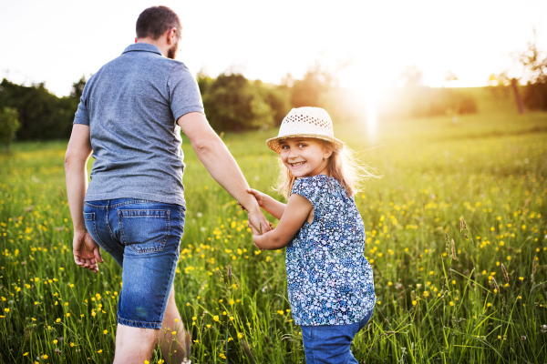 Father with a small daughter on a walk in sunny spring nature. Rear view.