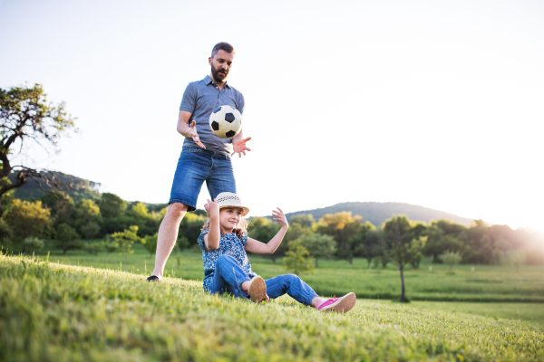 Father with a small daughter playing with a ball in sunny spring nature.