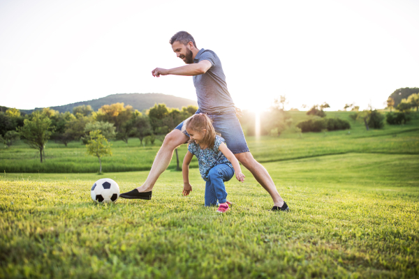 Happy father with a small daughter playing with a ball in spring nature at sunset.