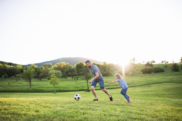 Father with a small daughter playing with a ball in sunny spring nature.