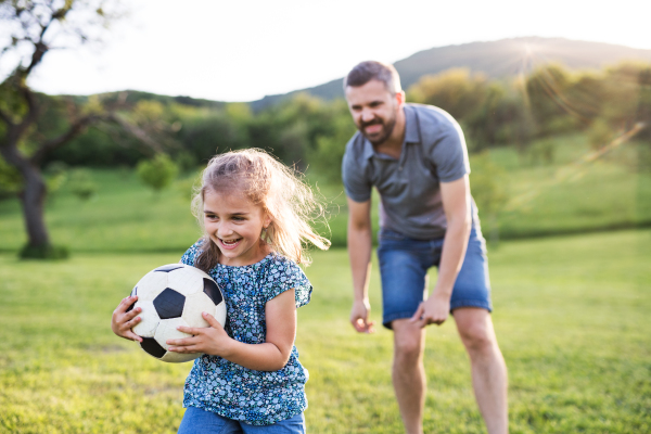 Father with a small daughter playing with a ball in sunny spring nature.