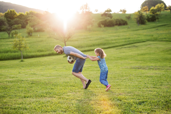 Happy father with a small daughter playing with a ball in spring nature at sunset.