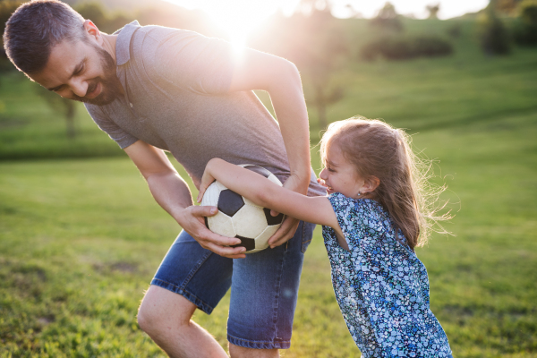 Father with a small daughter playing with a ball in spring nature at sunset.