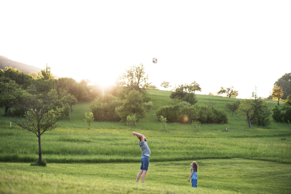 Father with a small daughter playing with a ball in spring nature at sunset.