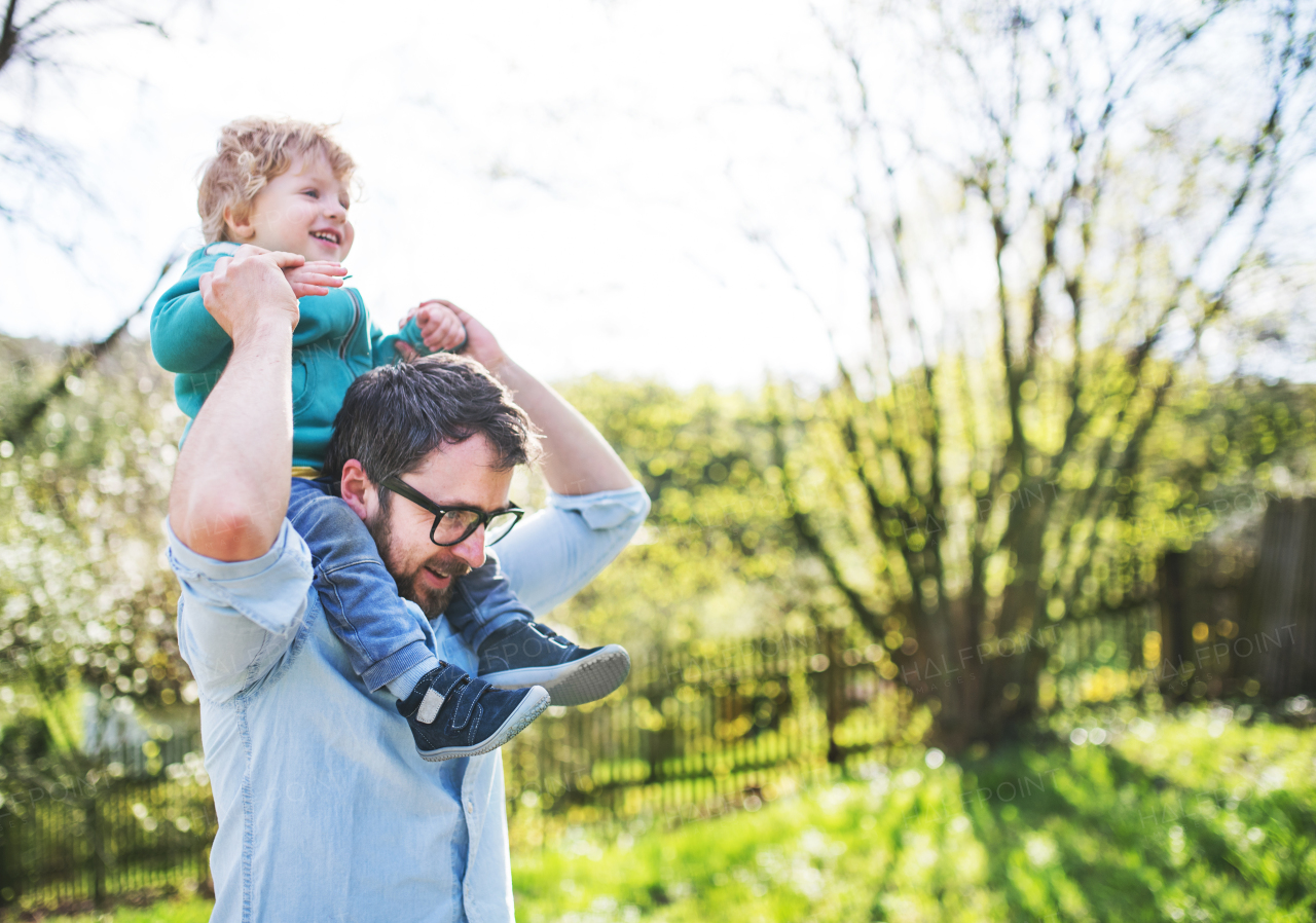 A father with his toddler son outside in green sunny spring nature, having fun. Copy space.