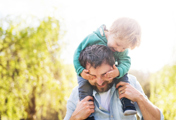 A father with his toddler son outside in green sunny spring nature, having fun.