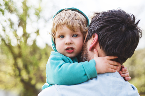 An unrecognizable father with his toddler son outside in green sunny spring nature, having fun.