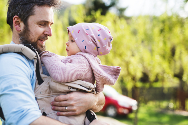 A father with his toddler daughter in a baby carrier outside on a spring walk. Copy space.