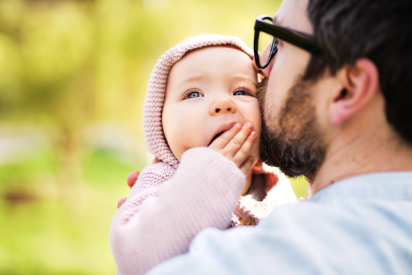 An unrecognizable father with his toddler daughter outside in green sunny spring nature, kissing.