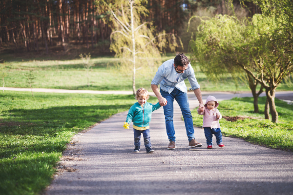 A father with his two toddler children outside on a sunny spring walk.