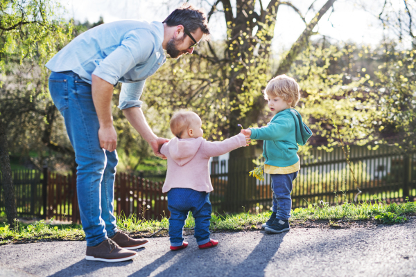 A father with his two toddler children outside on a sunny spring walk.