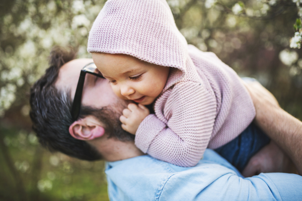 An unrecognizable father with his toddler daughter outside in green sunny spring nature, kissing.