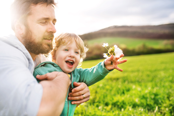 A father with his toddler son outside in green sunny spring nature.