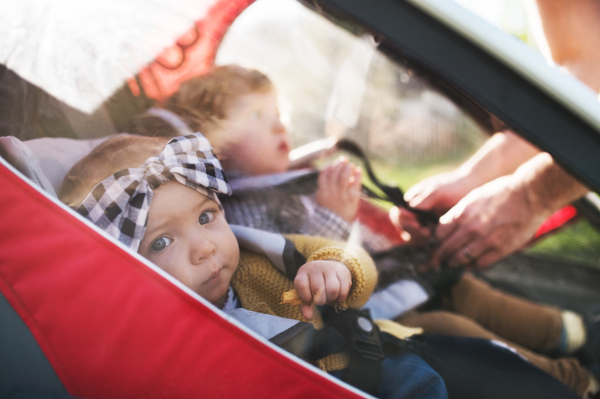 Unrecognizable father with two toddler children sitting in jogging stroller outside in spring nature. Close up.