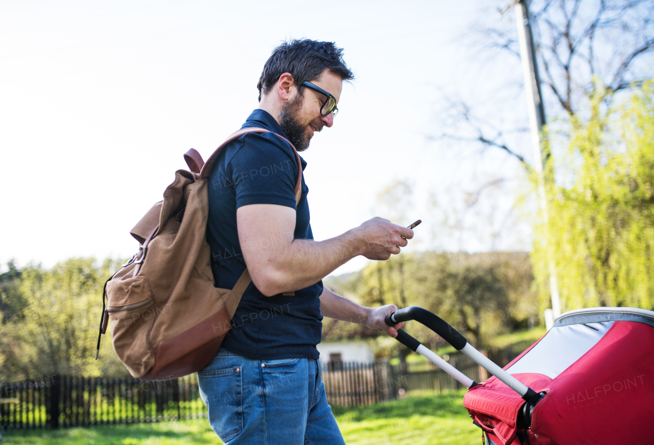 A father with backpack, smartphone and jogging stroller on a walk outside in spring nature.