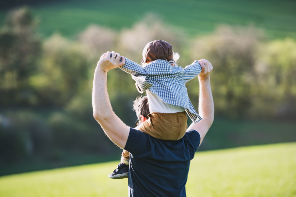 A father giving toddler son piggyback ride outside in spring nature. Rear view.