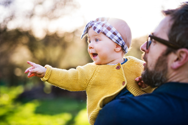 An unrecognizable father with his toddler daughter outside in green sunny spring nature.