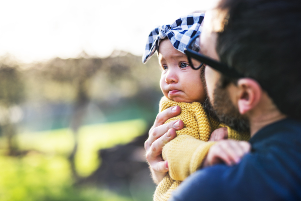 An unrecognizable father with his toddler daughter outside in green sunny spring nature. Copy space.