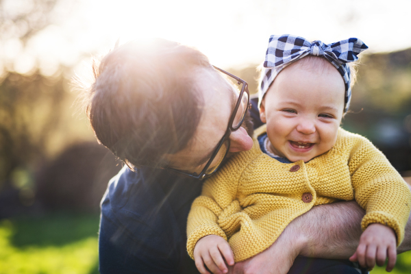 An unrecognizable father with his toddler daughter outside in green sunny spring nature.