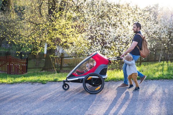 A father with toddler son pushing a jogging stroller outside. A walk in spring nature.