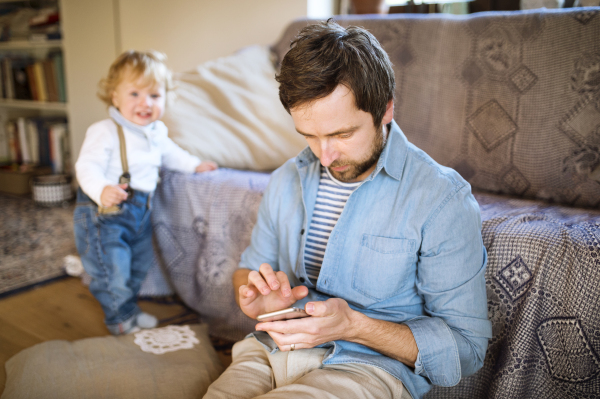 Young father with his son at home texting on sartphone.