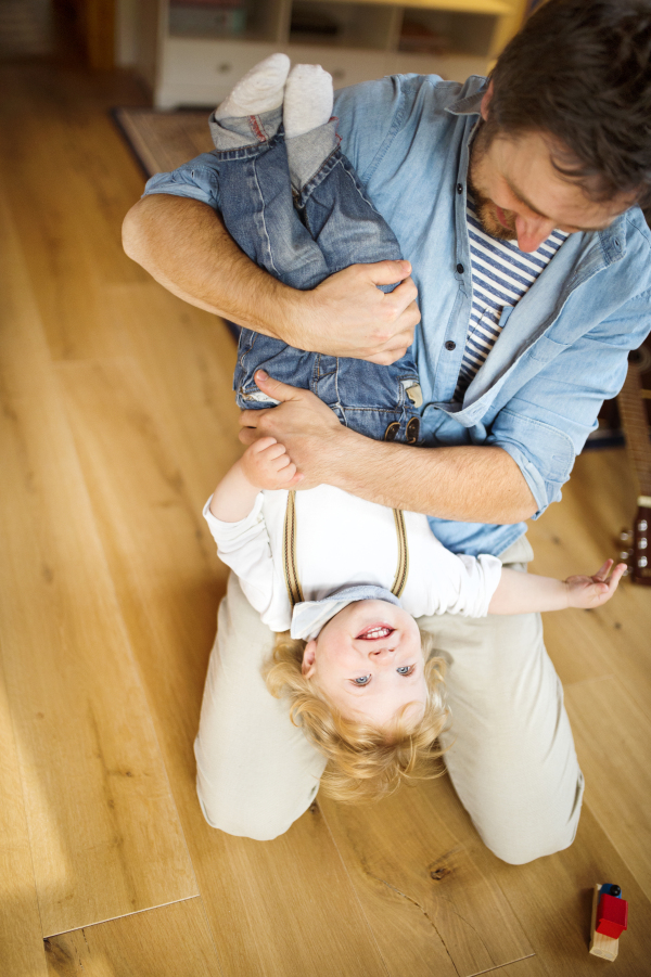 Young father at home playing with his little son, holding him upside down.