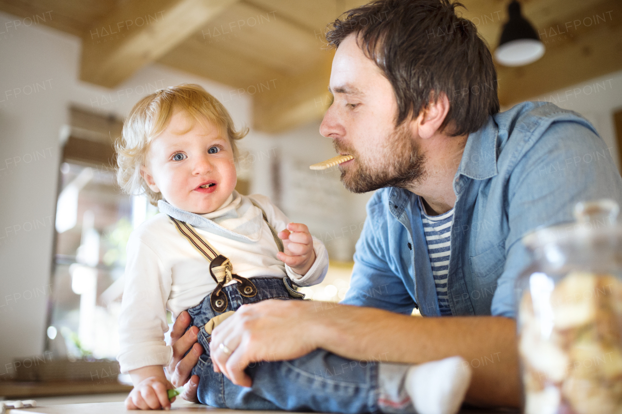 Young father at home with his cute little son eating biscuit together.