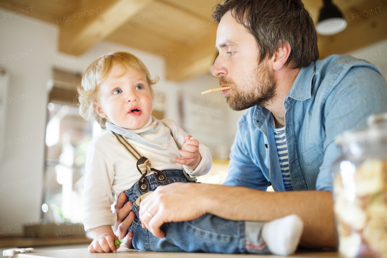 Young father at home with his cute little son eating biscuit together.