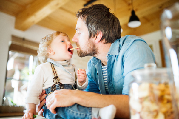 Young father at home with his cute little son eating biscuit together.