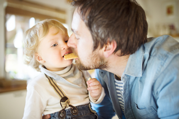 Young father at home with his cute little son eating biscuit together.