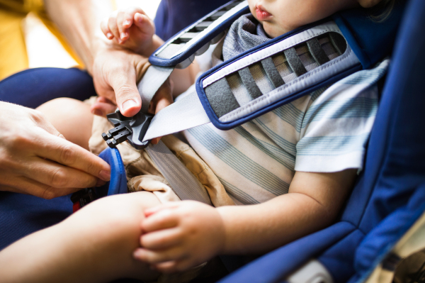 Unrecognizable father fastening seat belt for his son sitting in safety seat in the car.