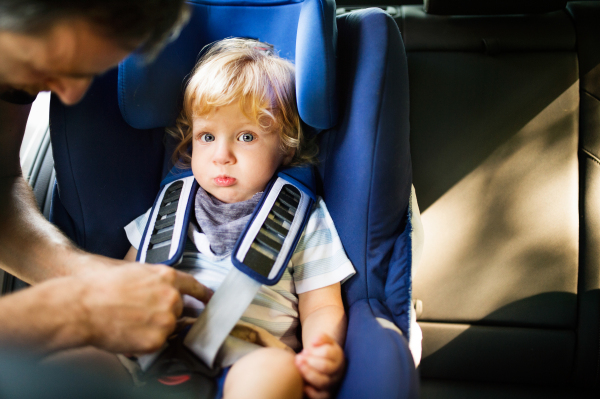 Unrecognizable father putting his son in the car. Toddler boy sitting in a car seat.