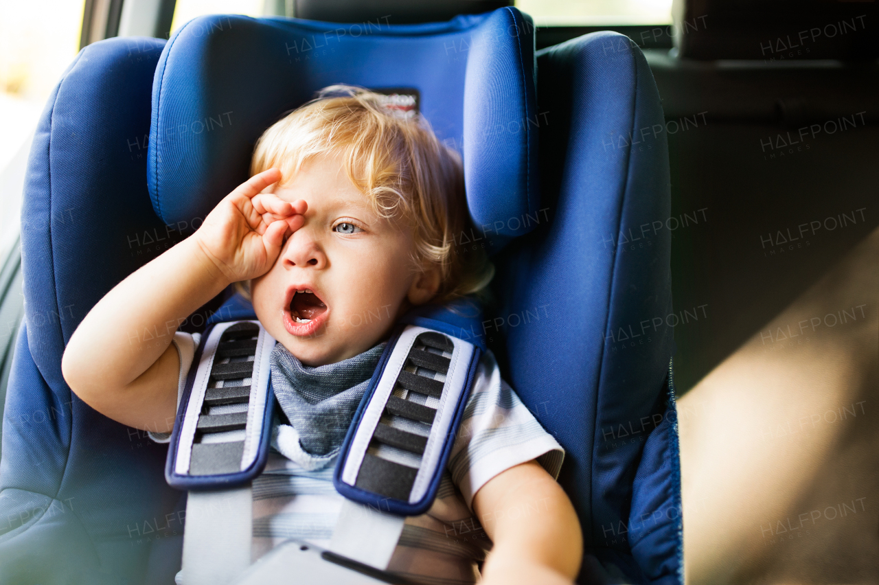 Cute little boy sitting in the car seat in the car, yawning.