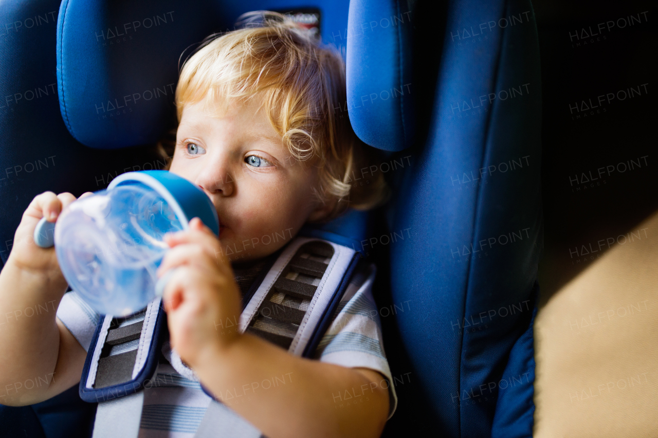 Cute little boy sitting in the car seat in the car. Toddler drinking from a baby cup. Close up.