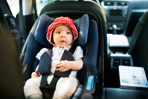 Cute little baby girl fastened with security belt in safety car seat.