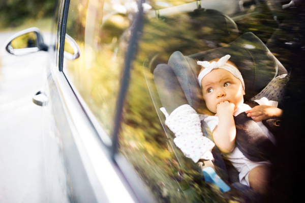 Cute little baby girl fastened with security belt in safety car seat. Shot through glass.