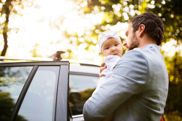 Young father holding his little baby girl in the arms going into the car.