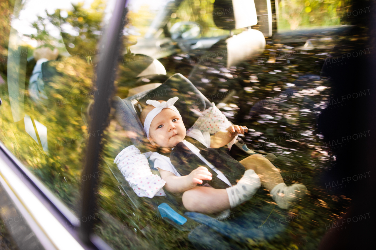 Cute little baby girl fastened with security belt in safety car seat. Shot through glass.