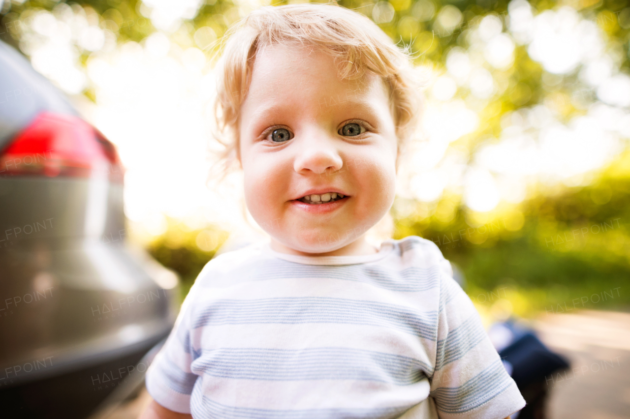 Cute little boy standing outside, by the car.