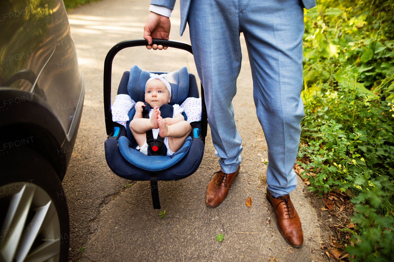 Unrecognizable man carrying his baby girl in a car seat. Man with a baby by the car.